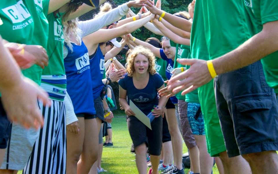 A teen girl runs in between parallel rows of adults joining hands to make a human tunnel.