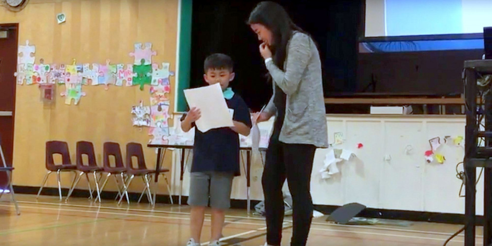 A young boy recites a poem while his older sister watches beside him.