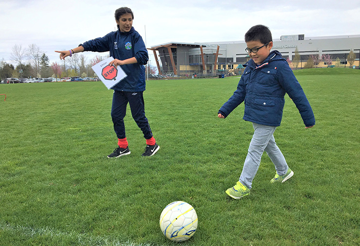 A young boy kicking a soccer ball with directions from a coach using visuals.