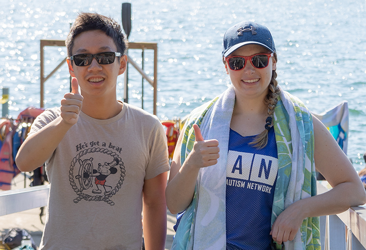 CAN participant and staff member stand smiling side by side with their thumbs up in front of a lake.